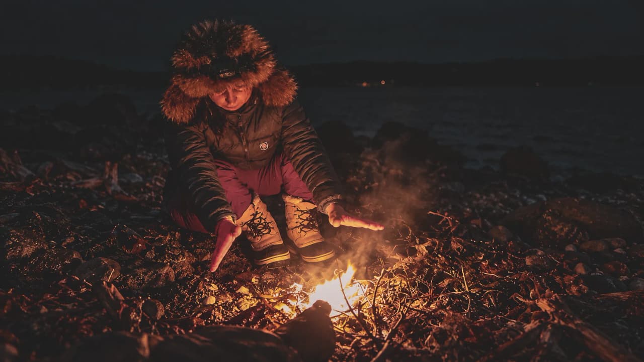 A person warming their hands by a campfire on a dark beach; a cosy atmosphere.