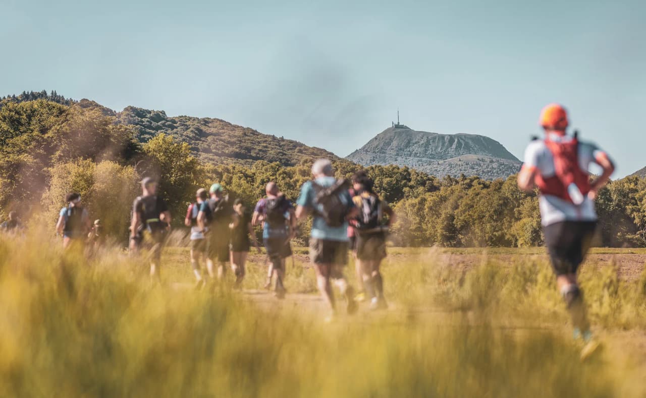 A group of runners on a green trail, with the majestic volcano range in the background.