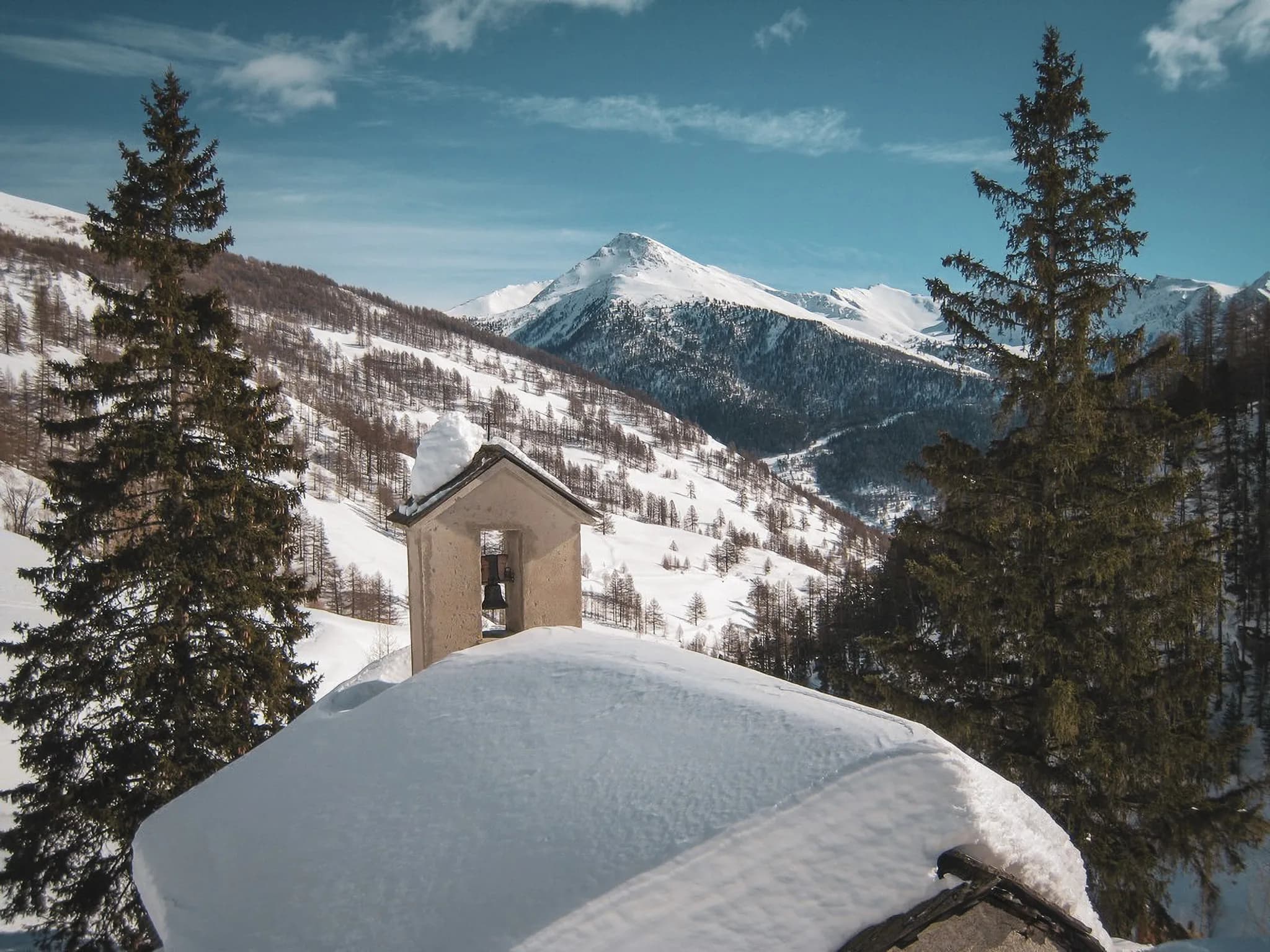 Panoramic view of the snow-capped Queyras mountains, with a picturesque bell tower.