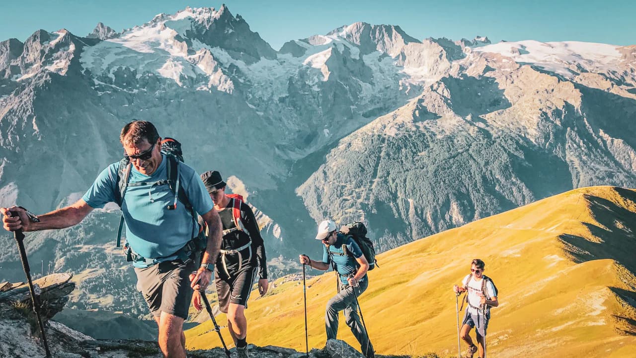 Groupe de randonneurs sur un sentier alpin, avec les aiguilles enneigées en arrière-plan.