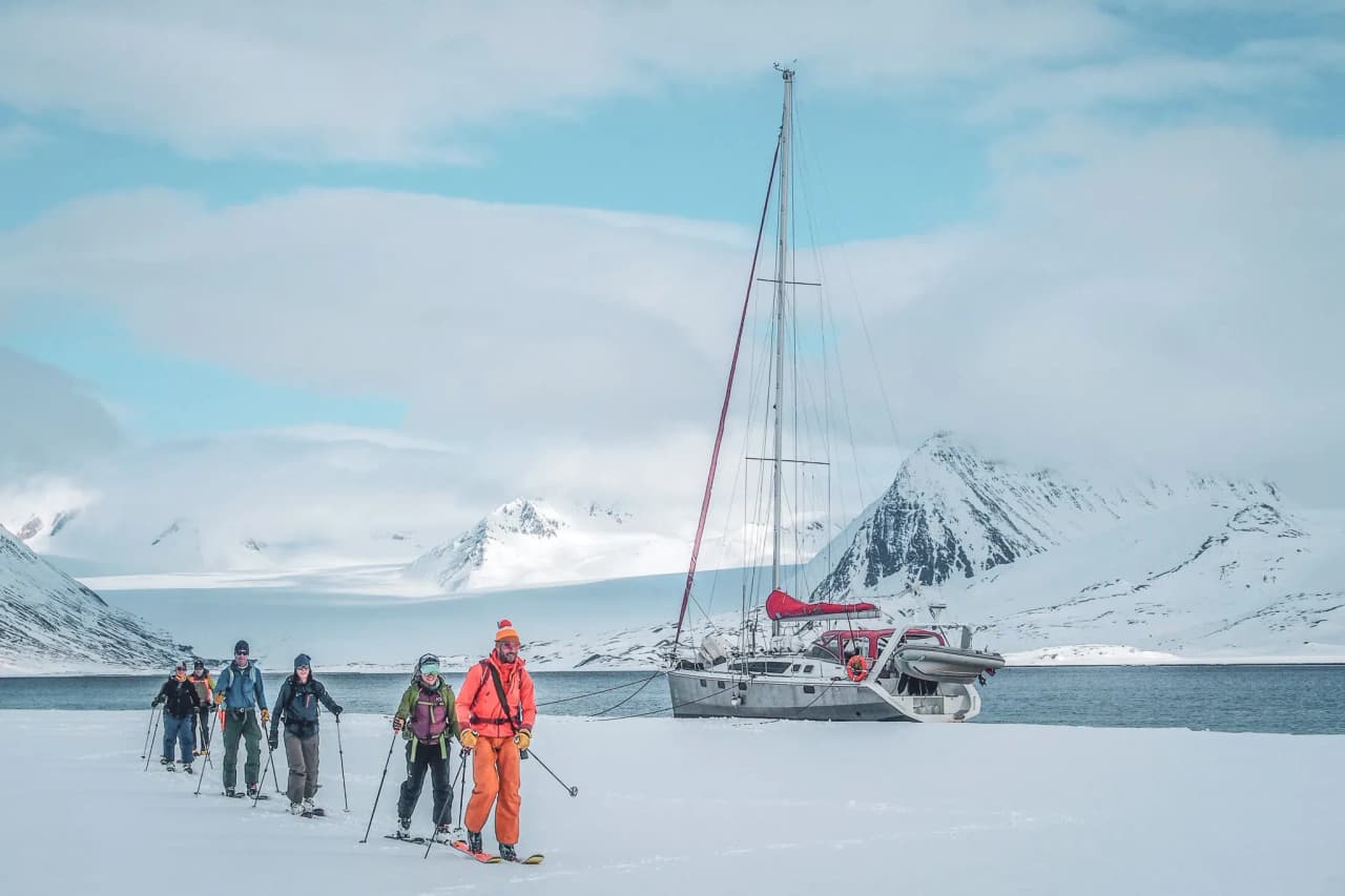 A group of ski-tourers make their way across the snow, with majestic mountains in the background.