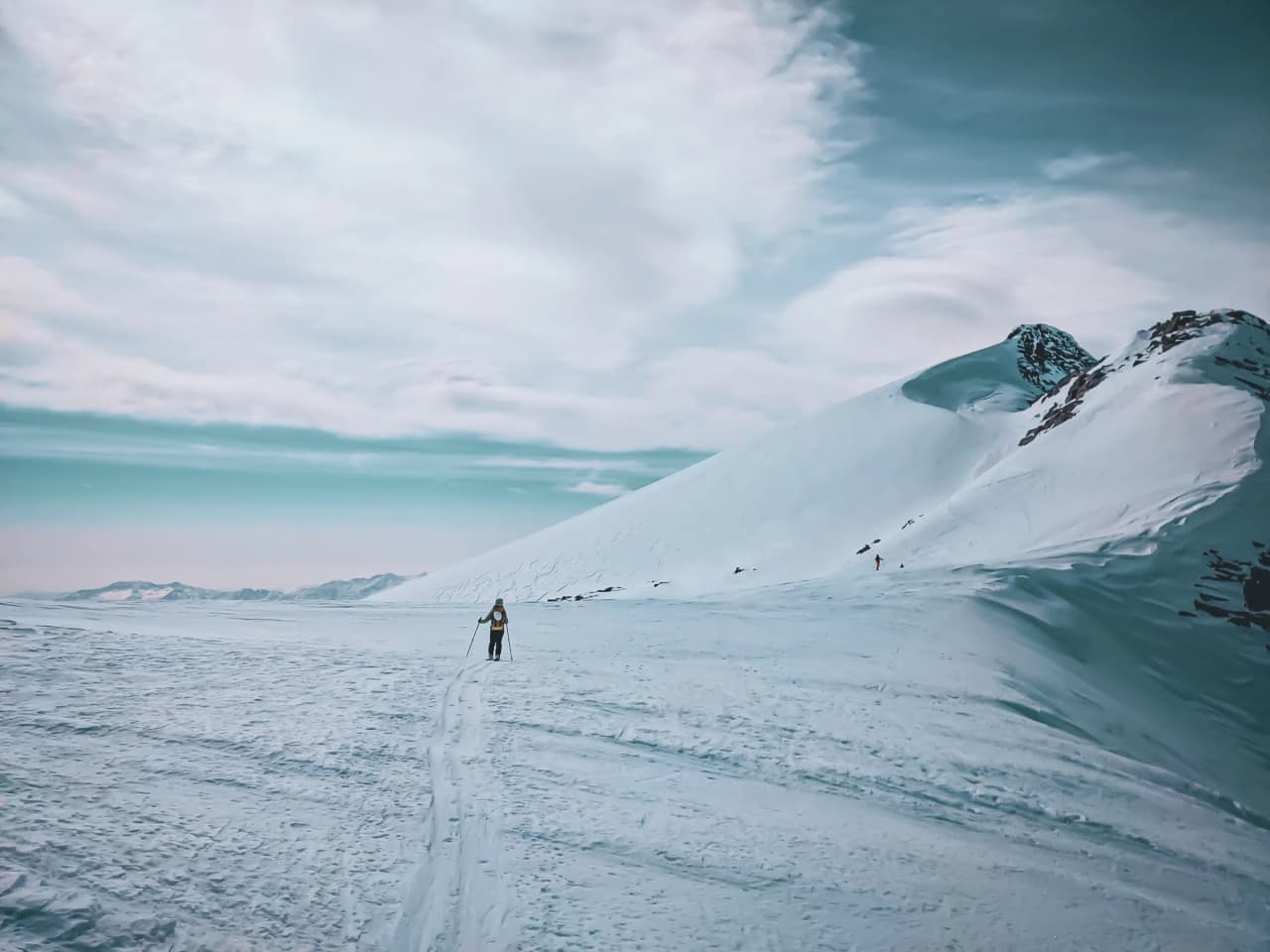 A lone skier on a vast glacier under a magnificent sky, ready for adventure.