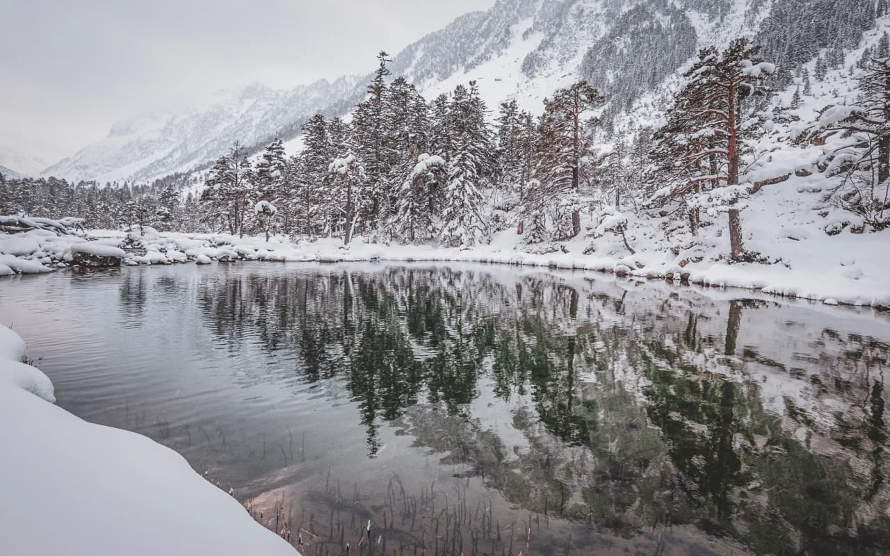 An enchanting landscape in the Pyrenees, a reflection of snow-covered forests on a peaceful lake.