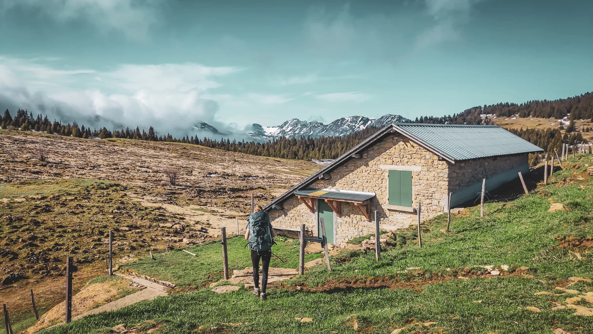 Randonneur se dirigant vers une charmante cabane en pierre, entourée de montagnes majestueuses.