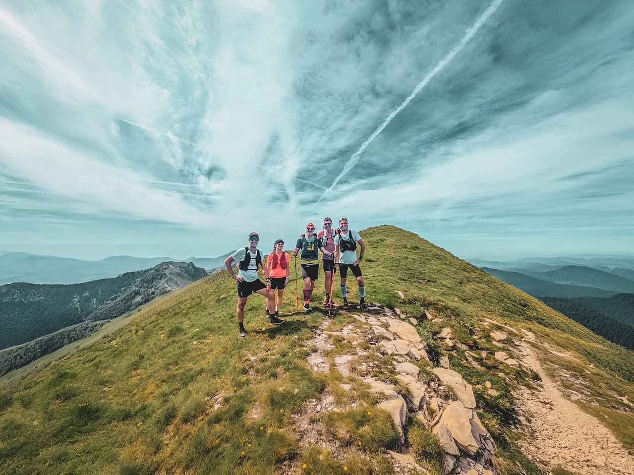 Groupe de traileurs souriants sur un sommet verdoyant, avec un ciel bleu magnifique en arrière-plan.