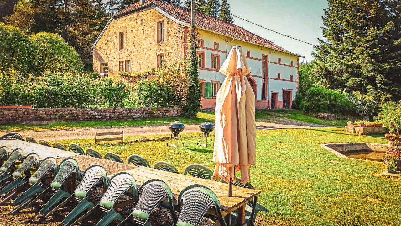 A charming corner of greenery with wooden tables, comfortable chairs and a stone house.