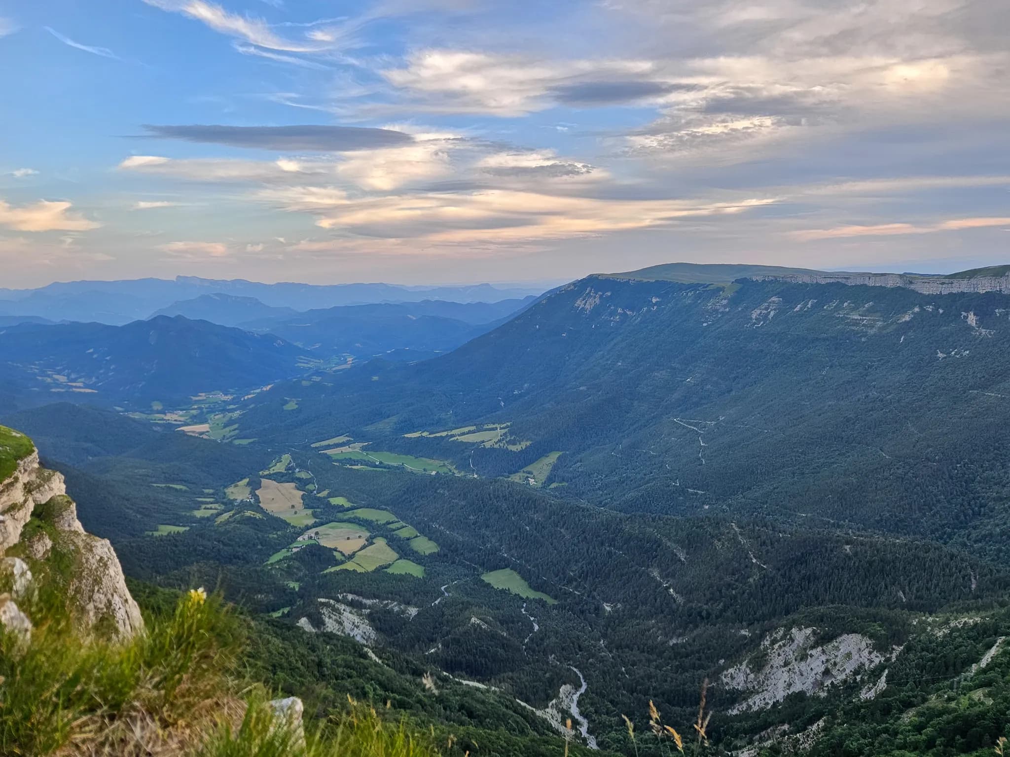 A majestic mountain landscape, with lush green valleys and rolling hills. In the foreground, rocky cliffs frame the view, while in the background, mountains stretch out to the horizon.