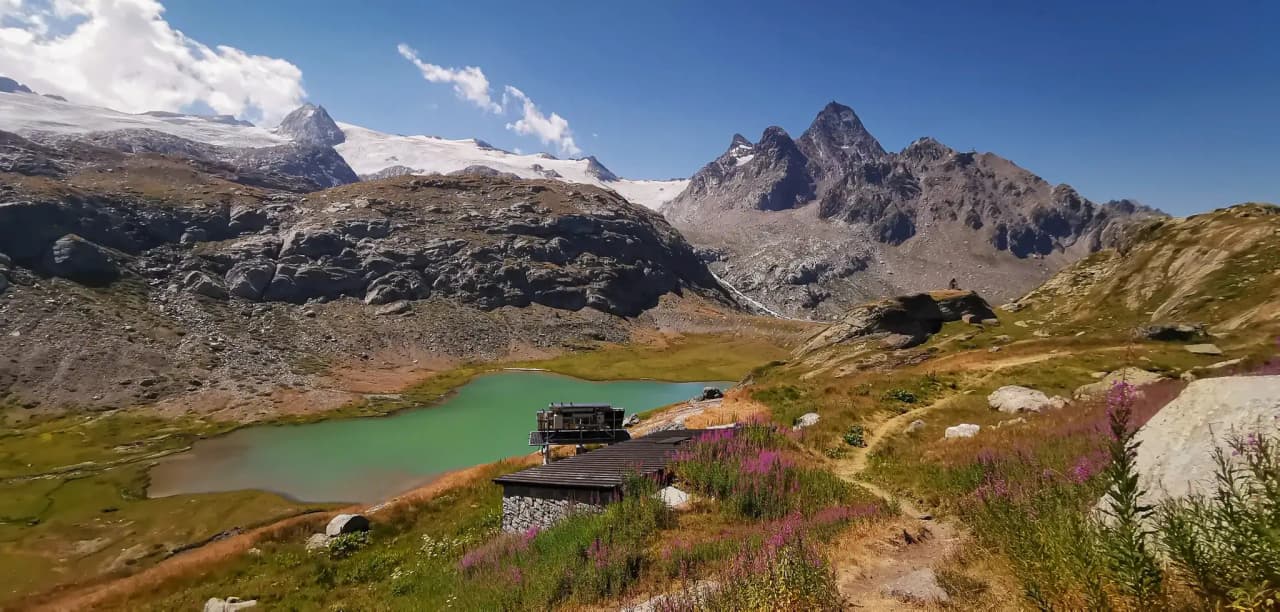 Un lac vert entouré de montagnes majestueuses, avec un chalet paisible en arrière-plan.
