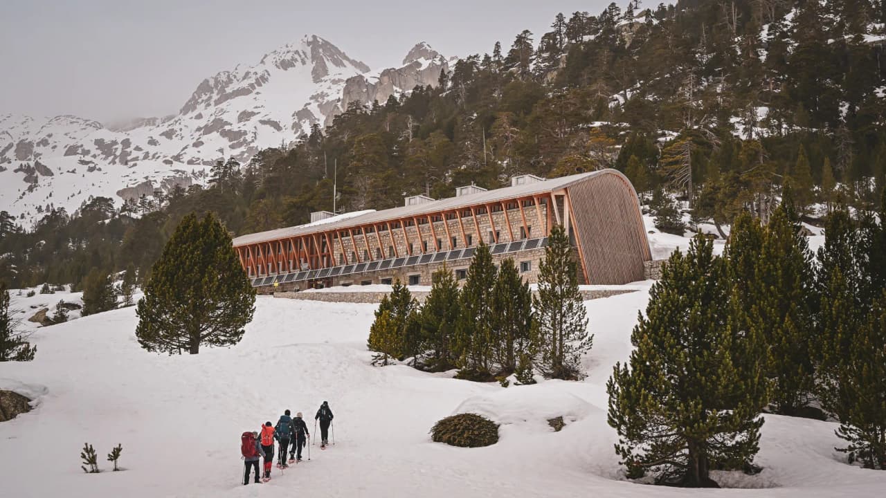 Group on snowshoes heading towards a modern Mountain hut in the snowy Pyrenees.
