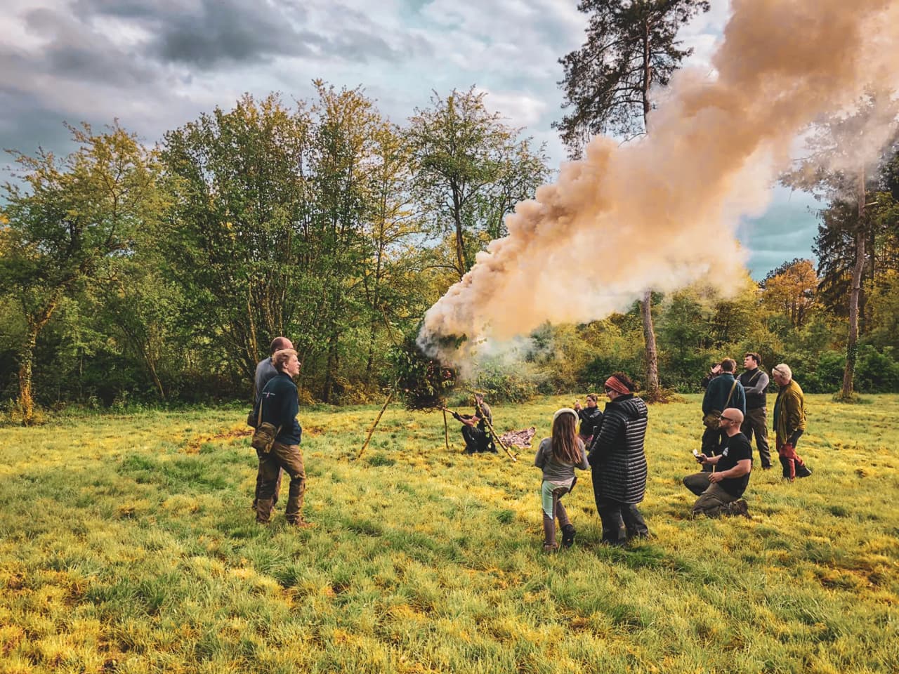 Groupe de participants en pleine activité de survie dans la forêt, avec de la fumée et des arbres verdoyants.
