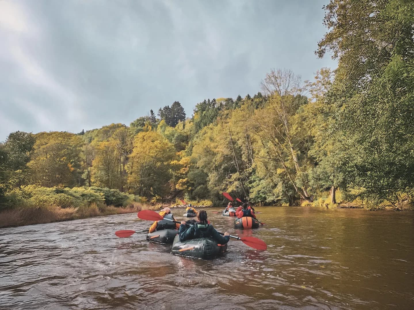 Group of packraft hikers navigating a river surrounded by colourful forests in the Ardennes.