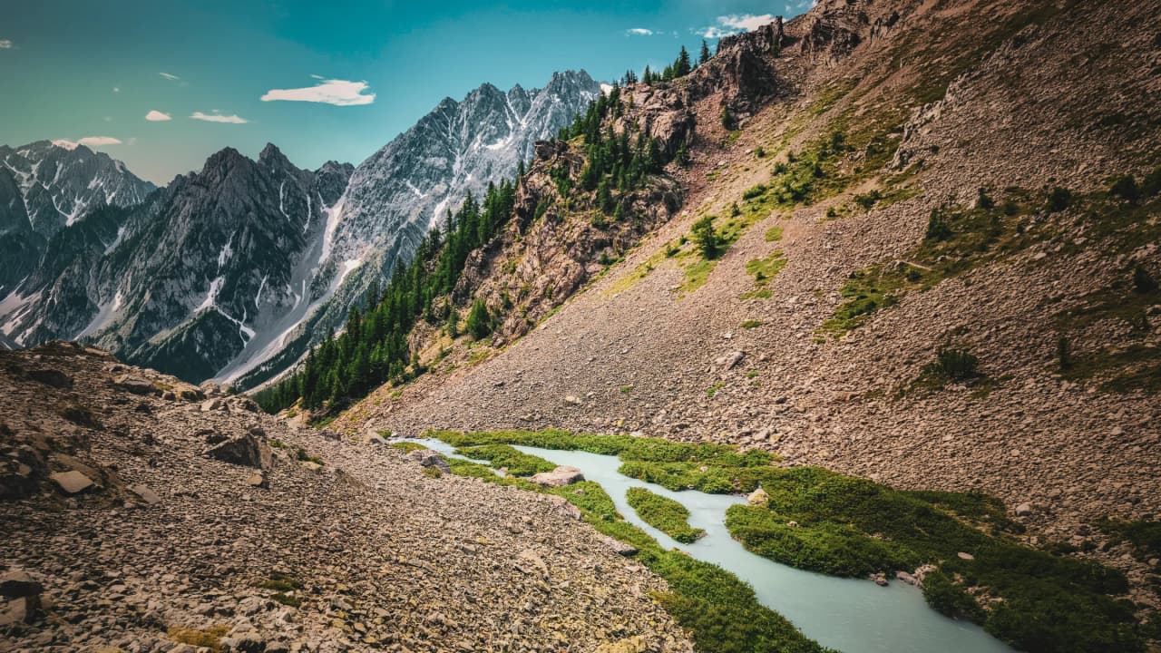 Vue panoramique des montagnes des Écrins, avec un cours d'eau serpentant et des paysages verdoyants.