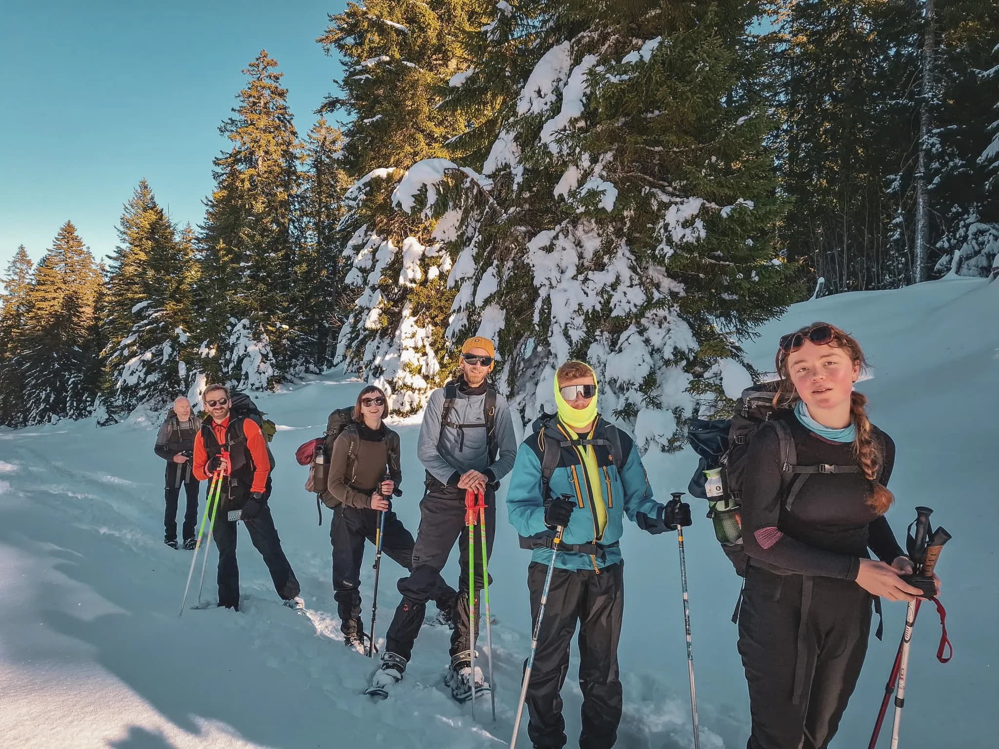 Een groep sneeuwschoenwandelaars in een besneeuwd landschap in de Zwitserse Jura, onder een blauwe hemel.