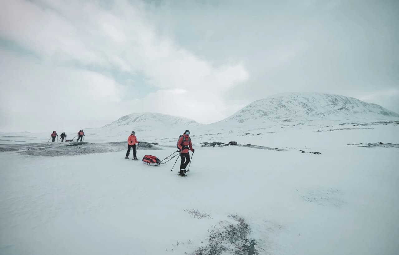Snowshoe expedition team on the snow, under heavy skies north of the Arctic Circle.