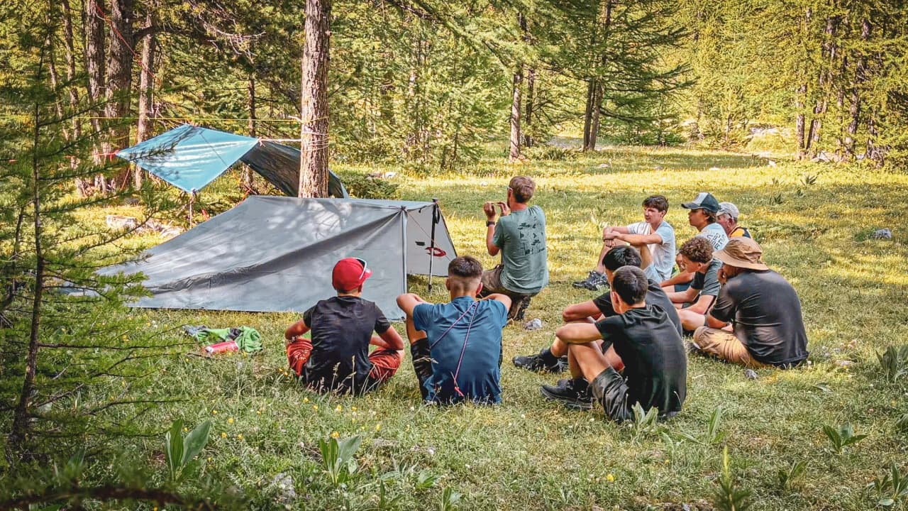 Groupe de jeunes assis sur l'herbe, apprenant des techniques de survie en pleine nature.