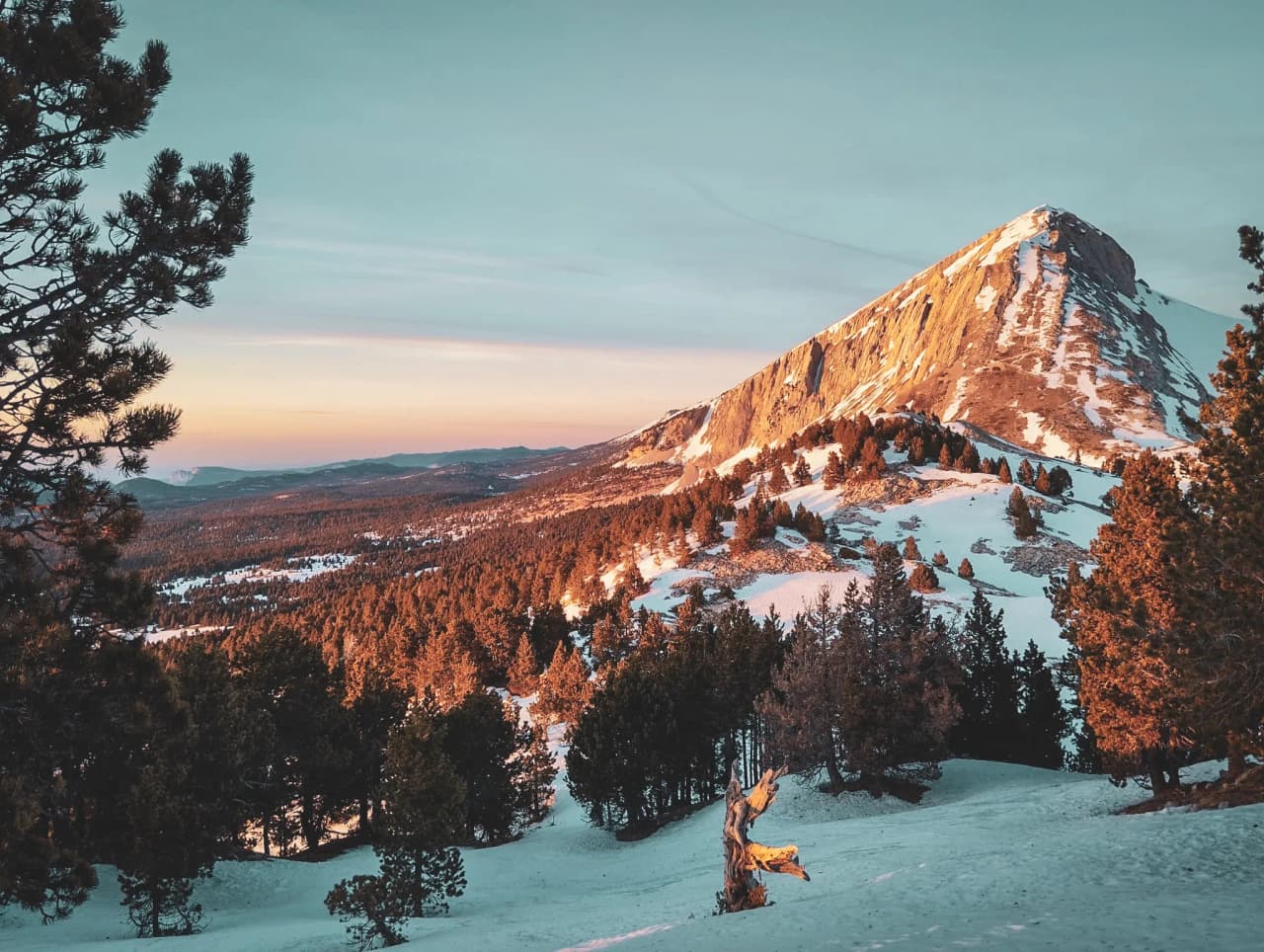 Snow-covered landscape of the Vercors, with Mont Aiguille on the horizon under a pastel sky. Looking for adventure?