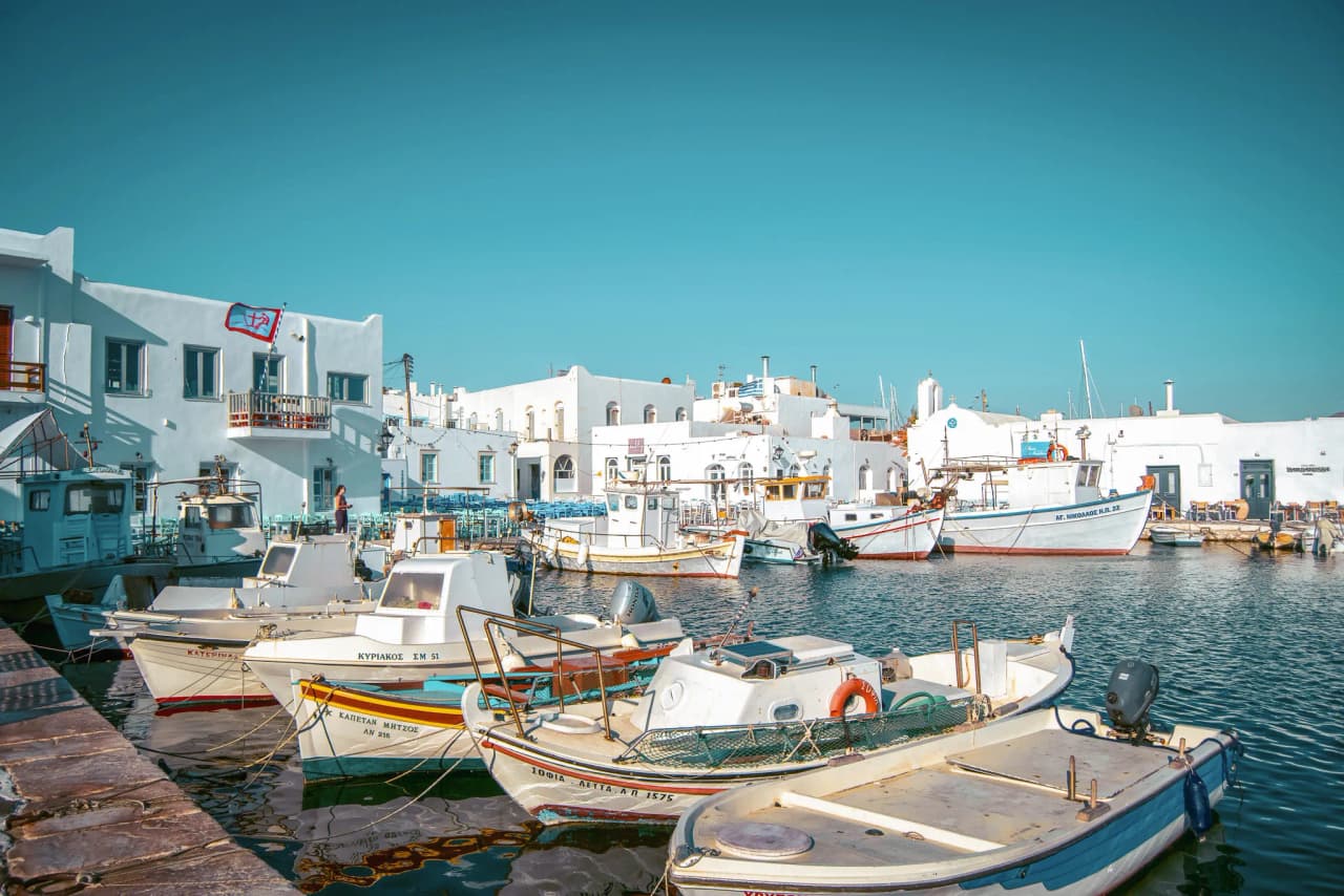 Port paisible des Cyclades avec des bateaux colorés, maisons blanches et ciel azur.
