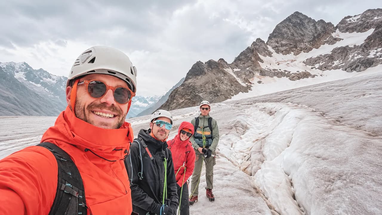 Quatre alpinistes souriants sur un glacier des Écrins, prêts à gravir des sommets majestueux.