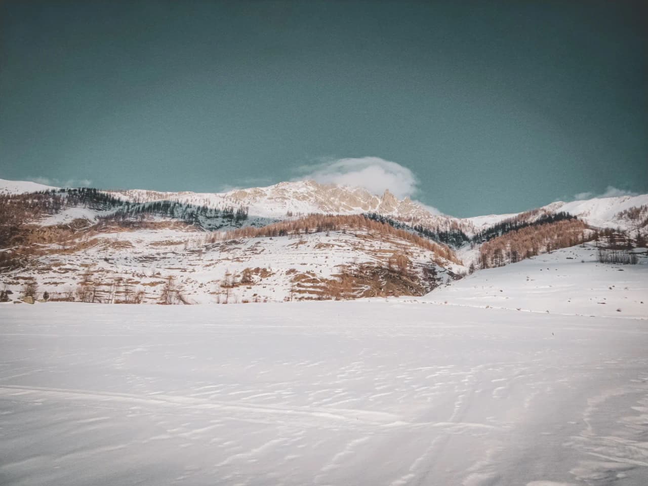 Een uitgestrekt, besneeuwd Alpenlandschap, majestueuze bergen onder een zachte hemel, een uitnodiging tot avontuur.