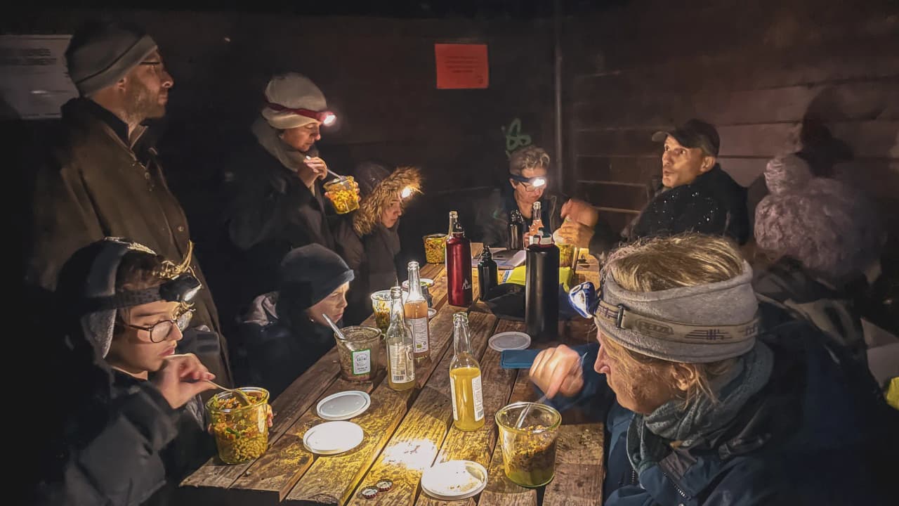 Groupe autour d'une table en pleine nuit, savourant des plats chauds après une excursion en nature.