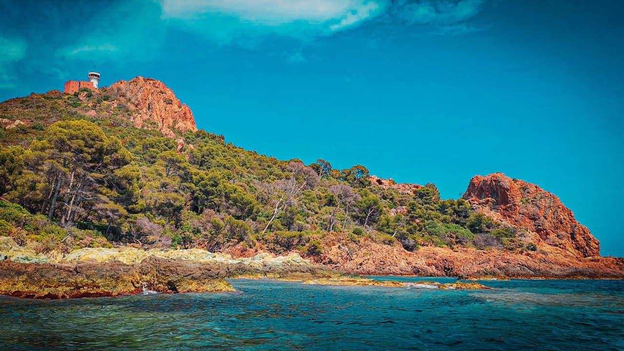 Schitterend mediterraan kustlandschap met rode rotsen, weelderig groen en stralend blauwe luchten.