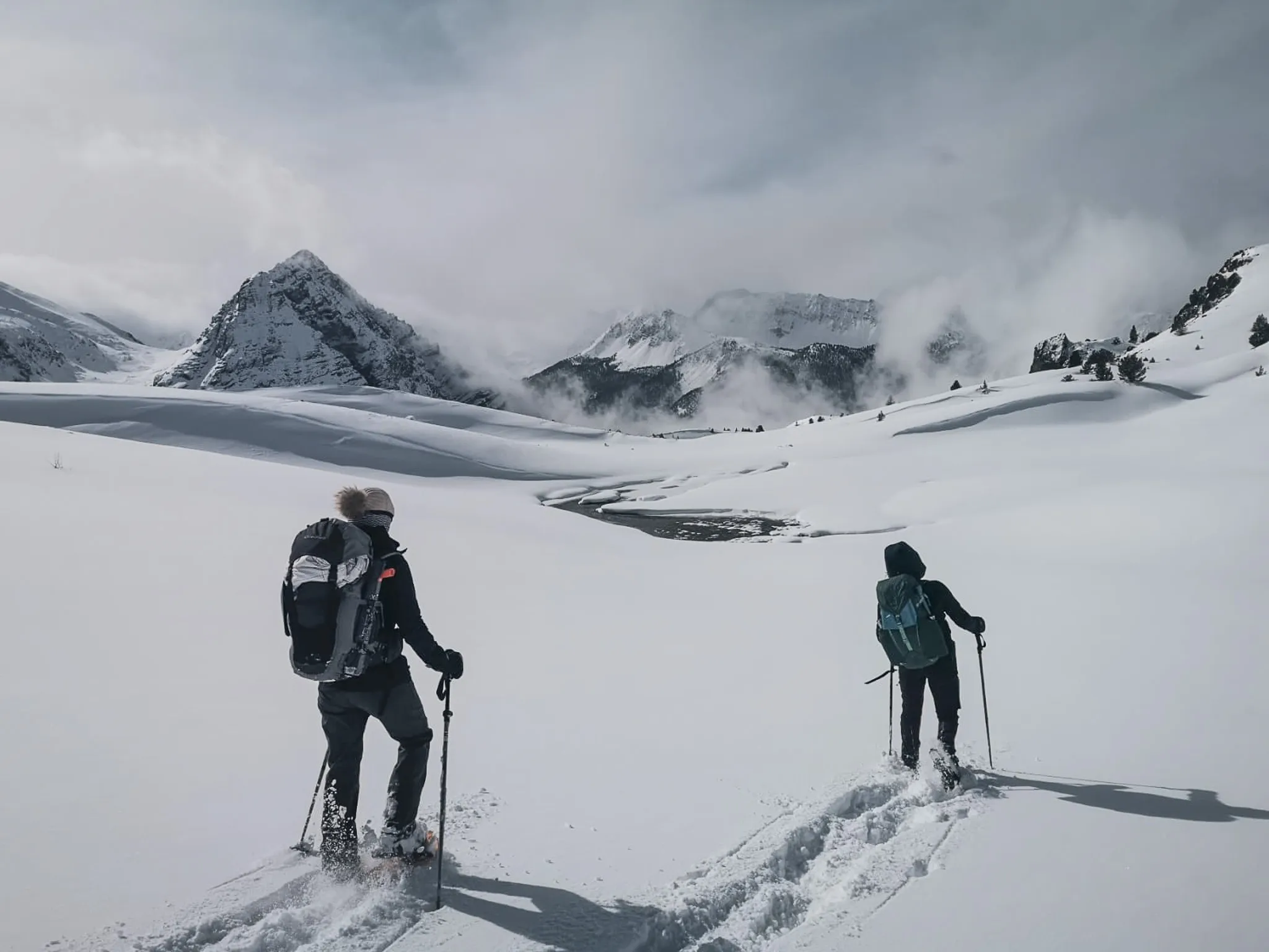 Two hikers on snowshoes in a snowy landscape, surrounded by majestic mountains.