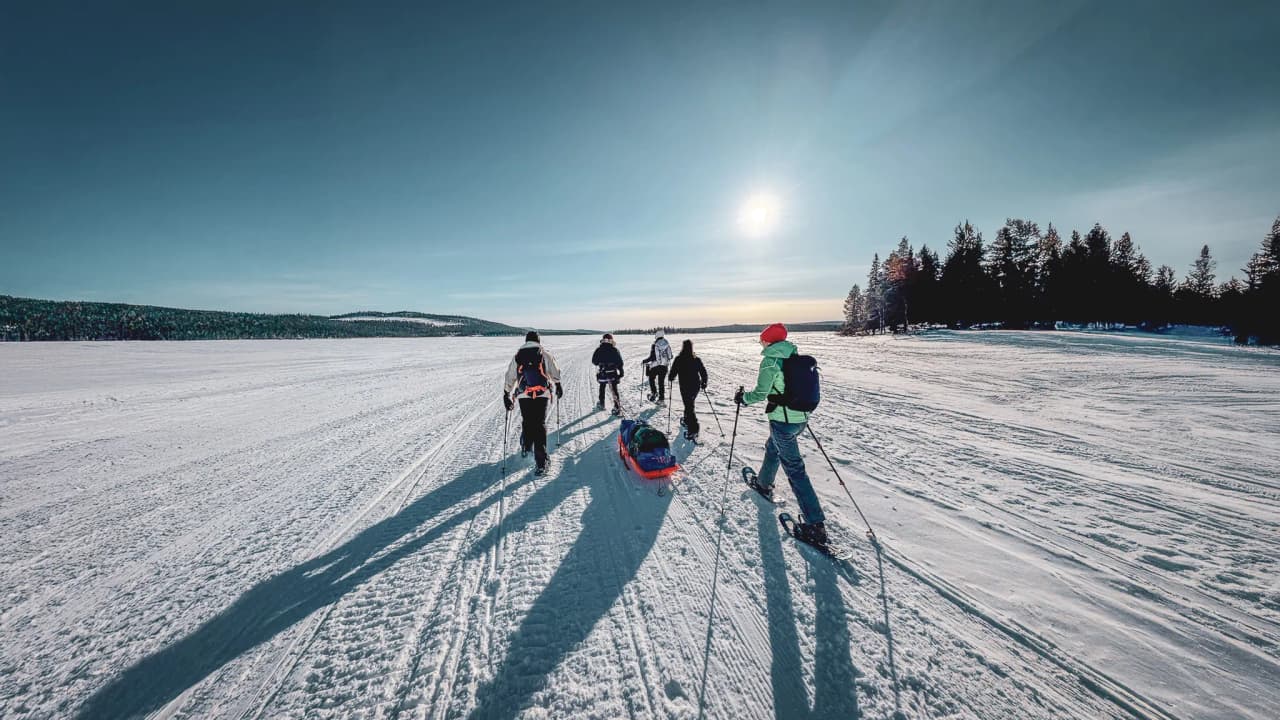 A group of explorers on snowshoes under a sunny sky in Lapland.