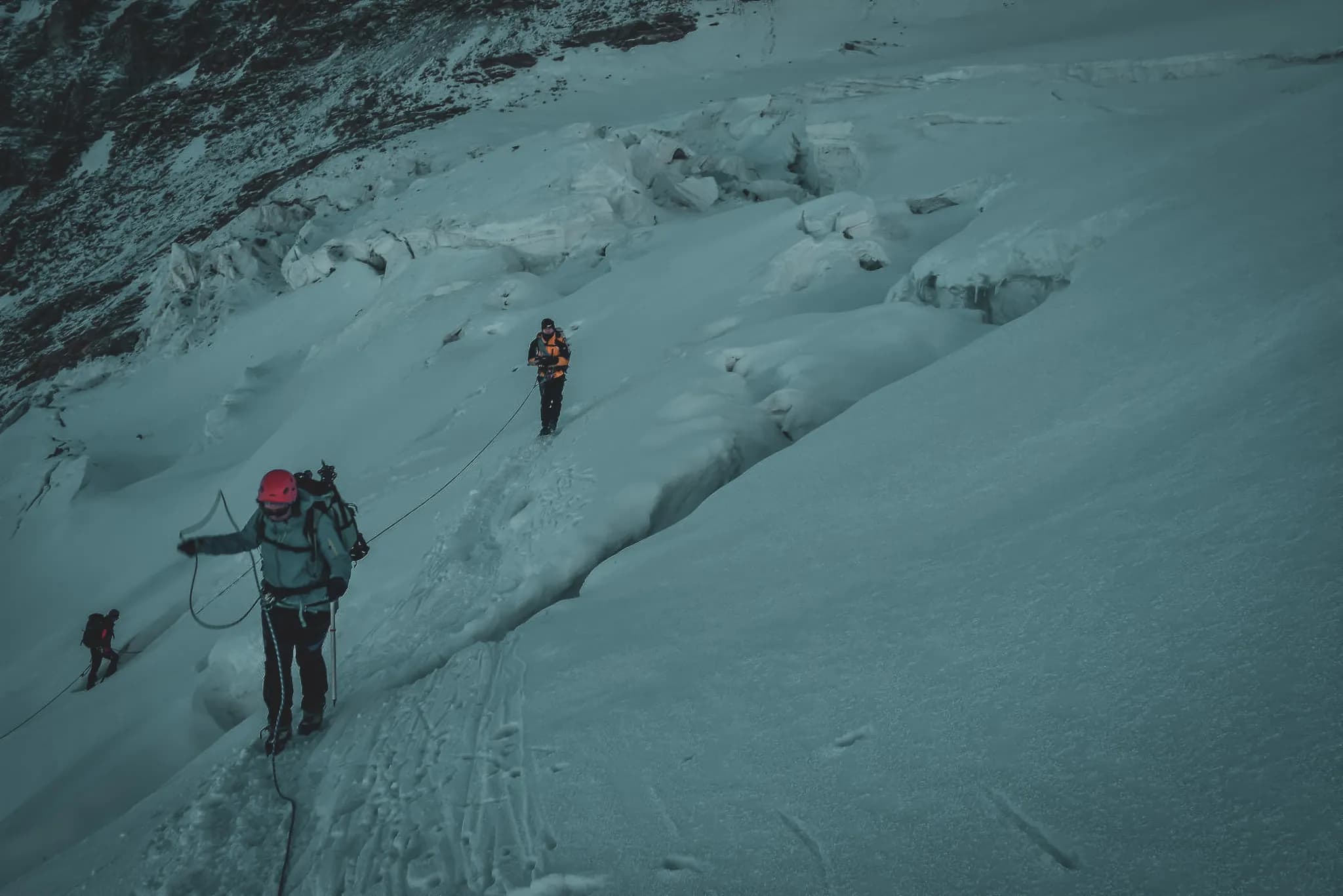 Een groep alpinisten beklimt Gran Paradiso over besneeuwde hellingen met ijs en zichtbare gletsjerspleten. Een klimmer met een roze helm leidt de tocht, goed uitgerust voor de uitdaging.