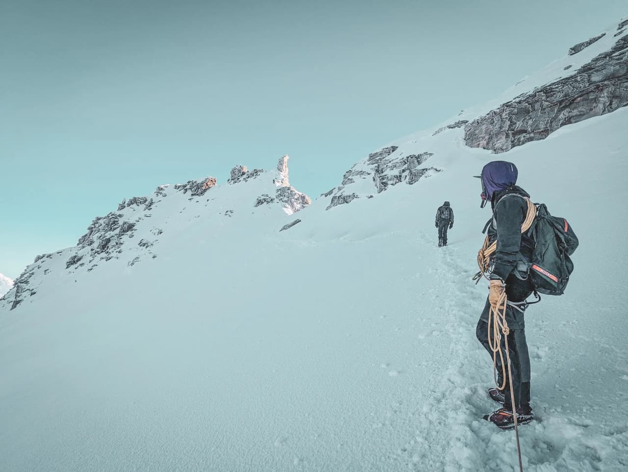Two mountaineers walk along a snowy path, surrounded by majestic mountains.