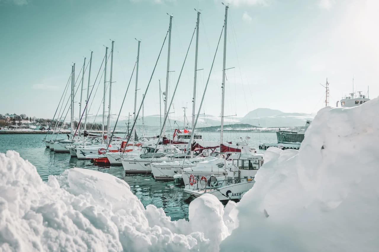 Lyngen Alpine harbour, sailing boats at anchor surrounded by glistening snow. A winter escape.