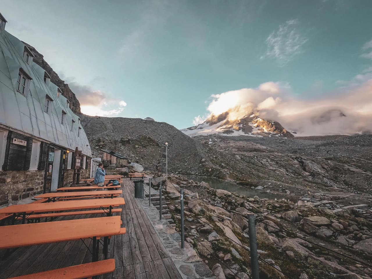 A mountain hut with wooden benches and the majestic Grand Paradis beneath the clouds.