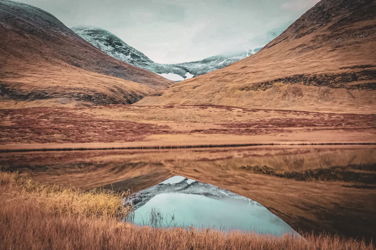 Golden valleys and snow-capped mountains reflected in a calm lake in Swedish Lapland.