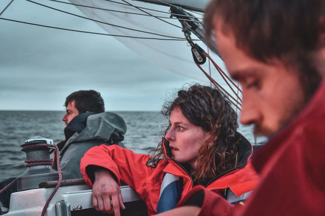 Three attentive sailors on a sailing boat at dawn, ready for an adventure at sea.