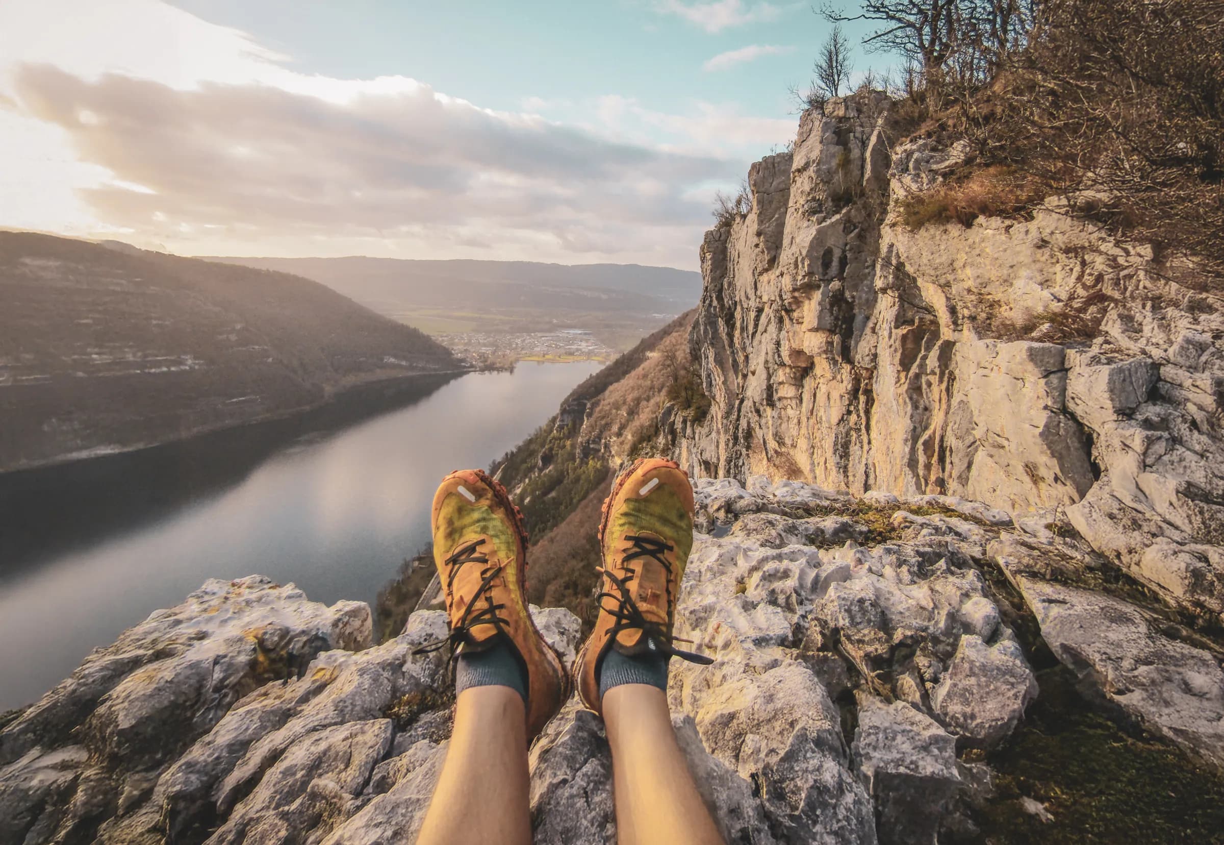 Pieds posés sur un rocher surplombant un lac et des montagnes sous un ciel bleu. Évasion en nature !
