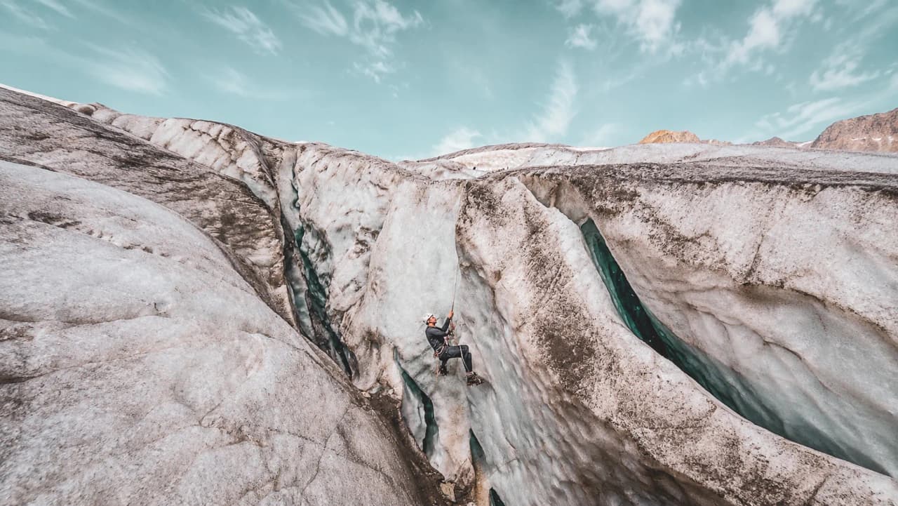 Un alpiniste grimpe sur un glacier majestueux sous un ciel bleu, prêt pour l'aventure.