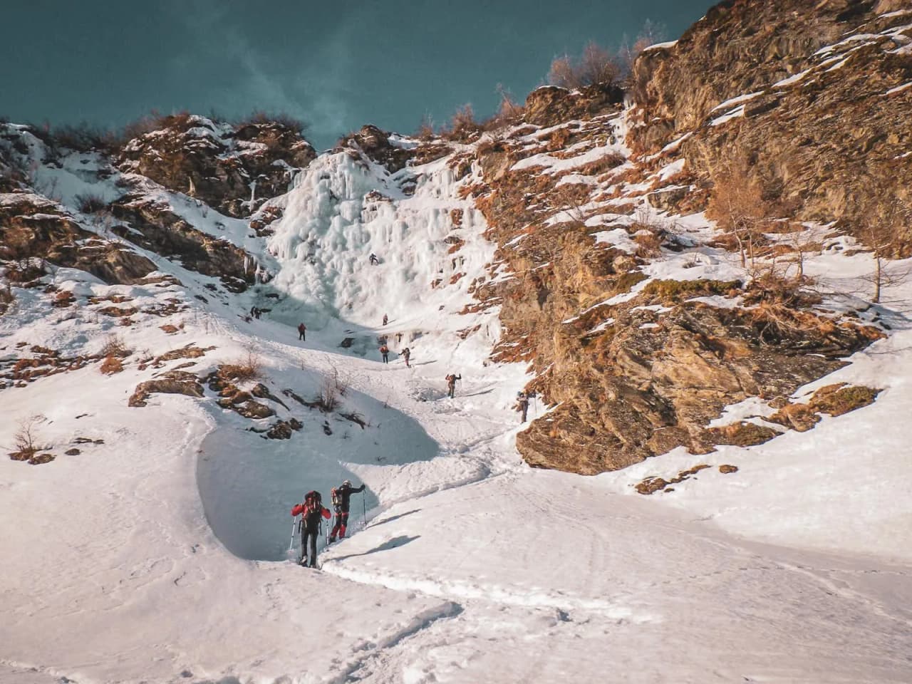 Des randonneurs escaladent une cascade de glace majestueuse dans les Alpes italiennes enneigées.