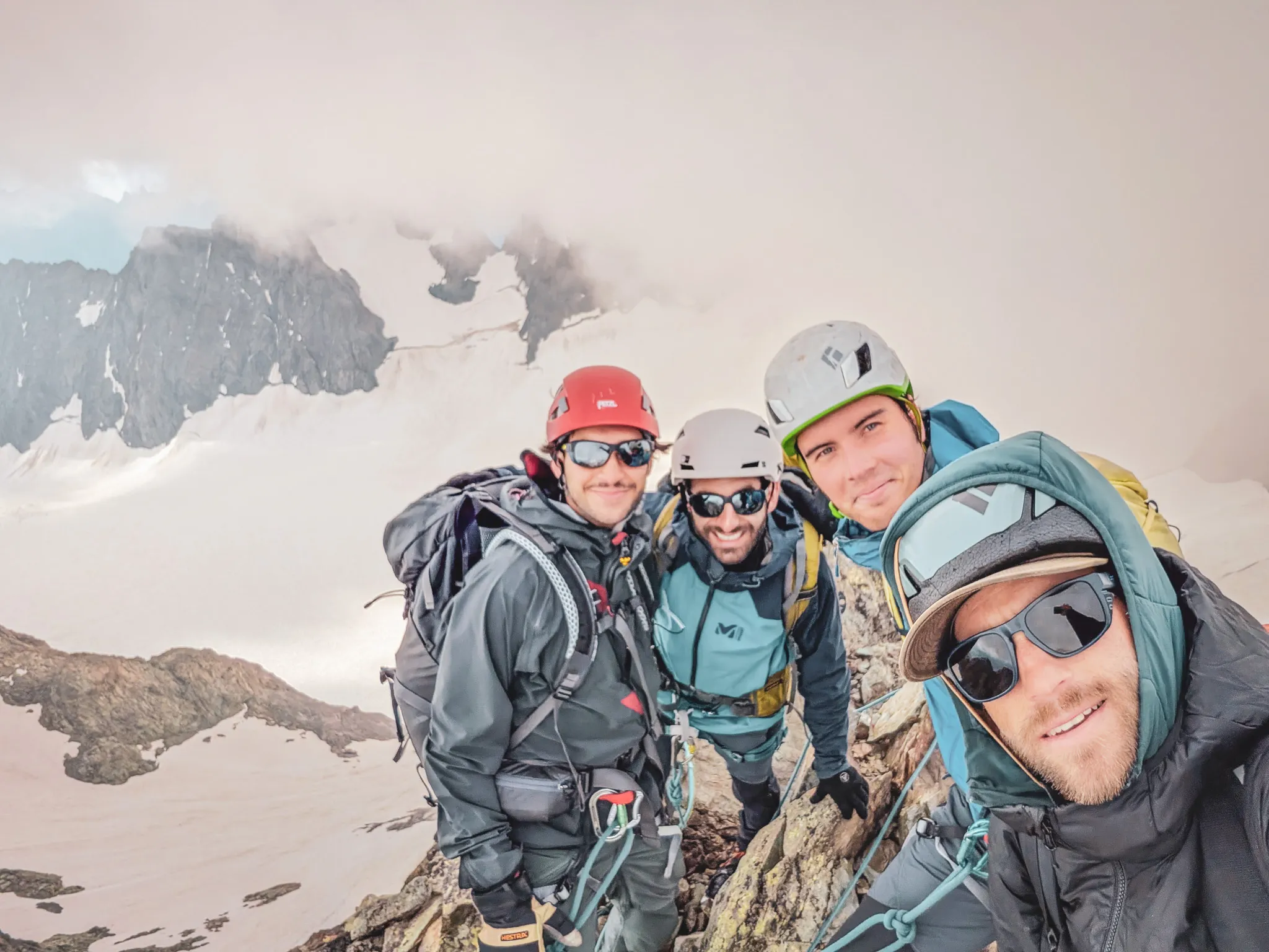Vier lachende klimmers poseren op de top van een berg, omringd door een majestueus landschap.