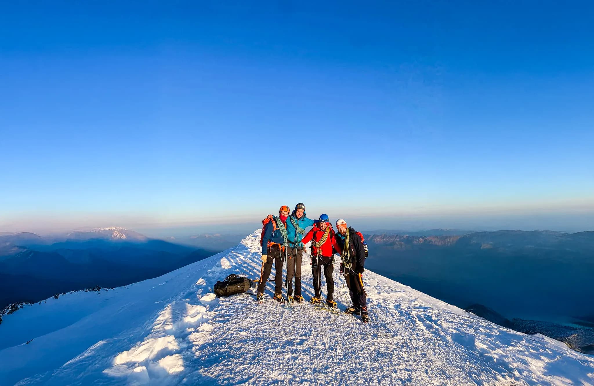 Cinq aventuriers joyeux, au sommet enneigé du Mont Blanc, sous un ciel bleu éclatant.
