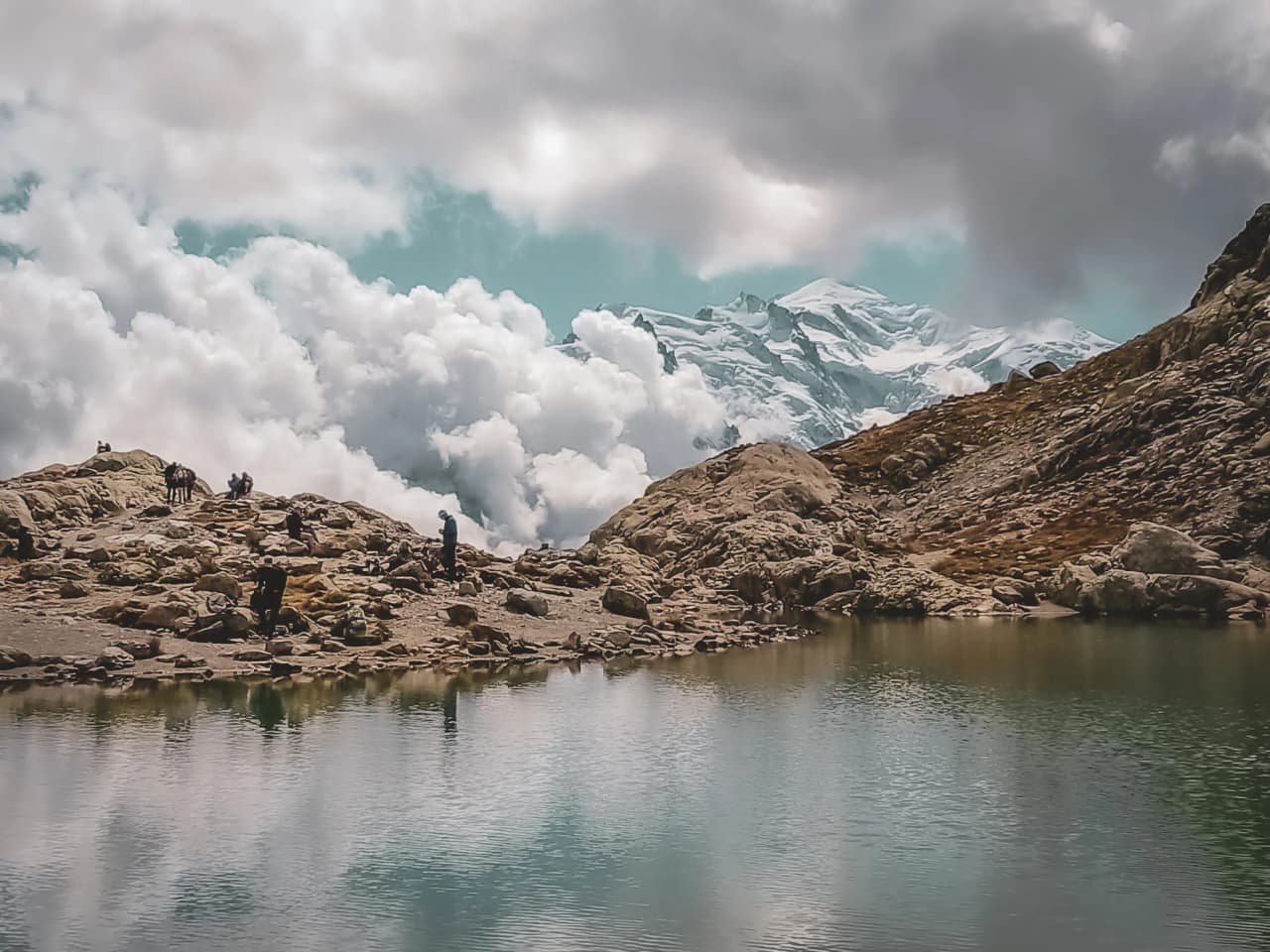 Un panorama alpin spectaculaire avec un lac glacial, des montagnes enneigées et des nuages majestueux.