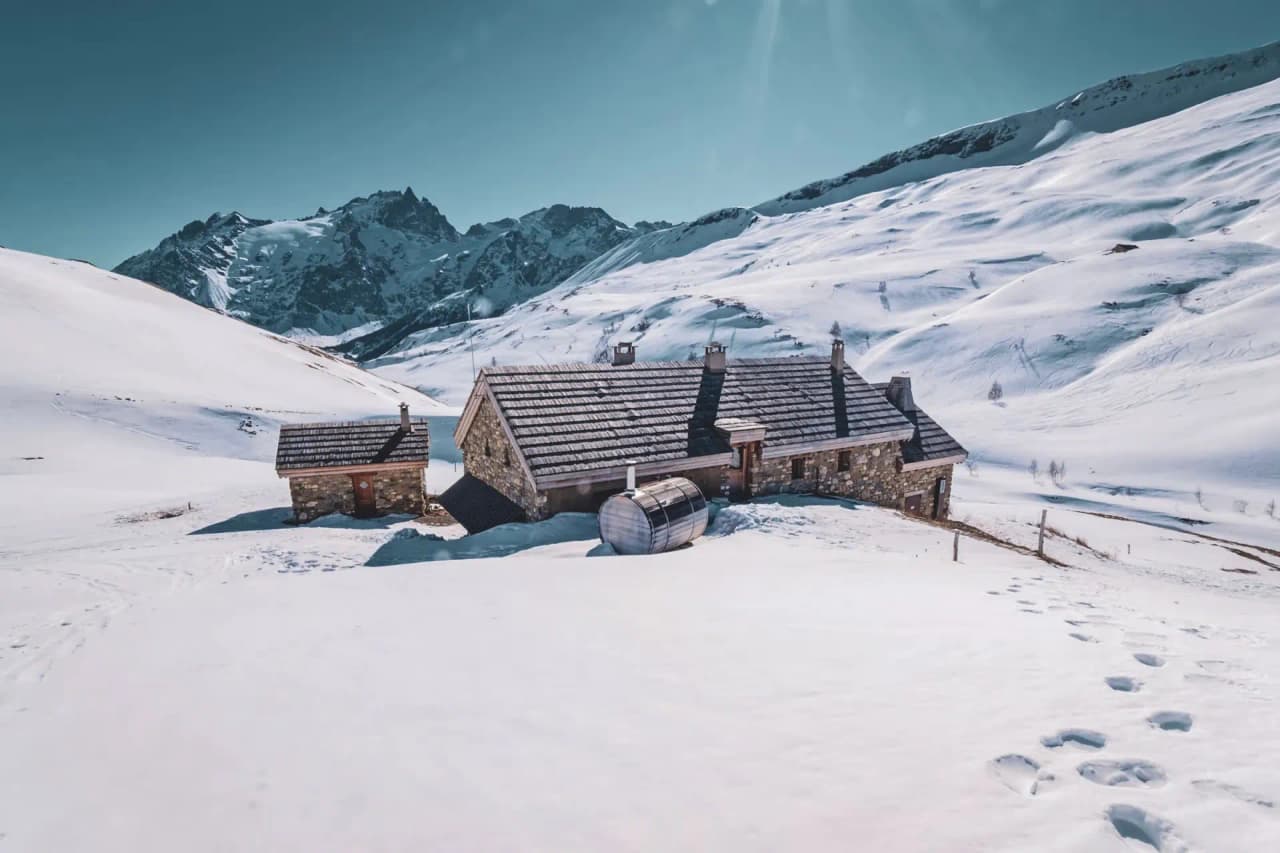 Un refuge en pierre entouré de neige immaculée et de montagnes majestueuses, invitation à l'aventure.
