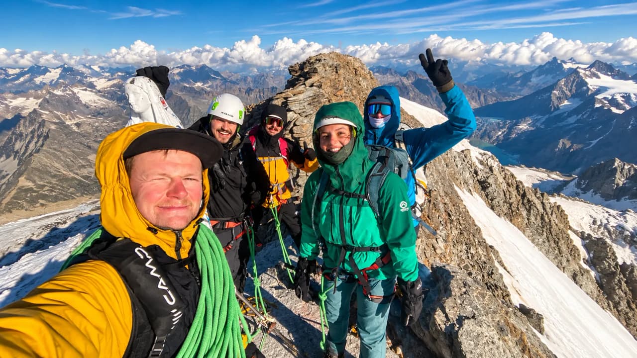 Groupe d'alpinistes au sommet avec des paysages montagneux spectaculaires en arrière-plan.