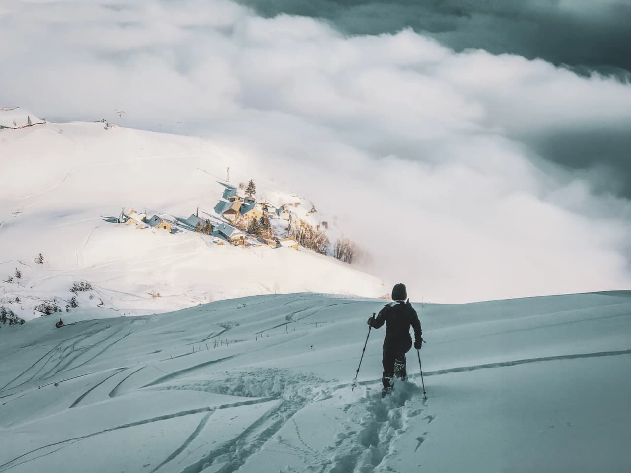 Randonneur en raquettes sur des neiges immaculées, avec vue sur un village dans les nuages.
