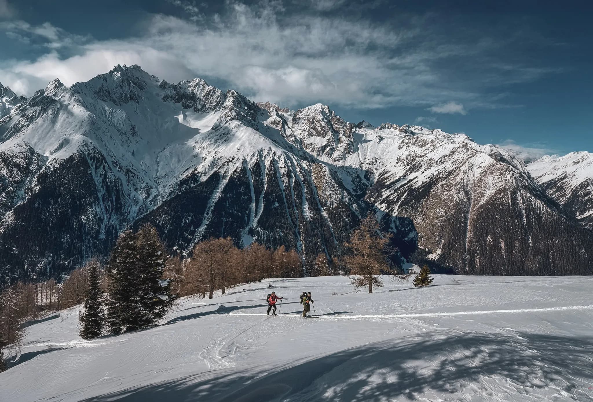 Two skiers explore a pristine alpine landscape, surrounded by majestic snow-capped mountains.