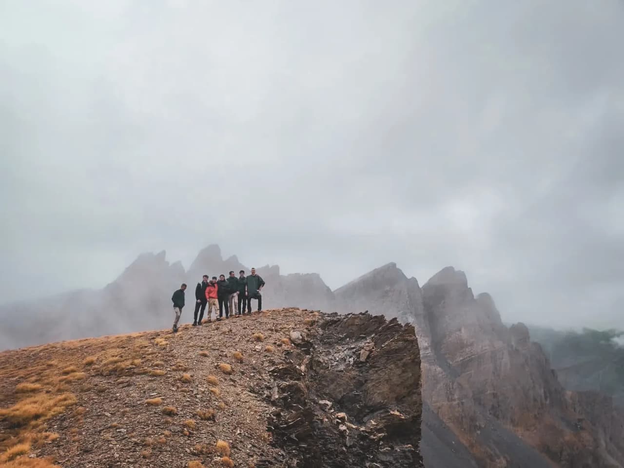 Groupe de randonneurs sur une crête alpine, entourés de majestueux sommets embrumés.