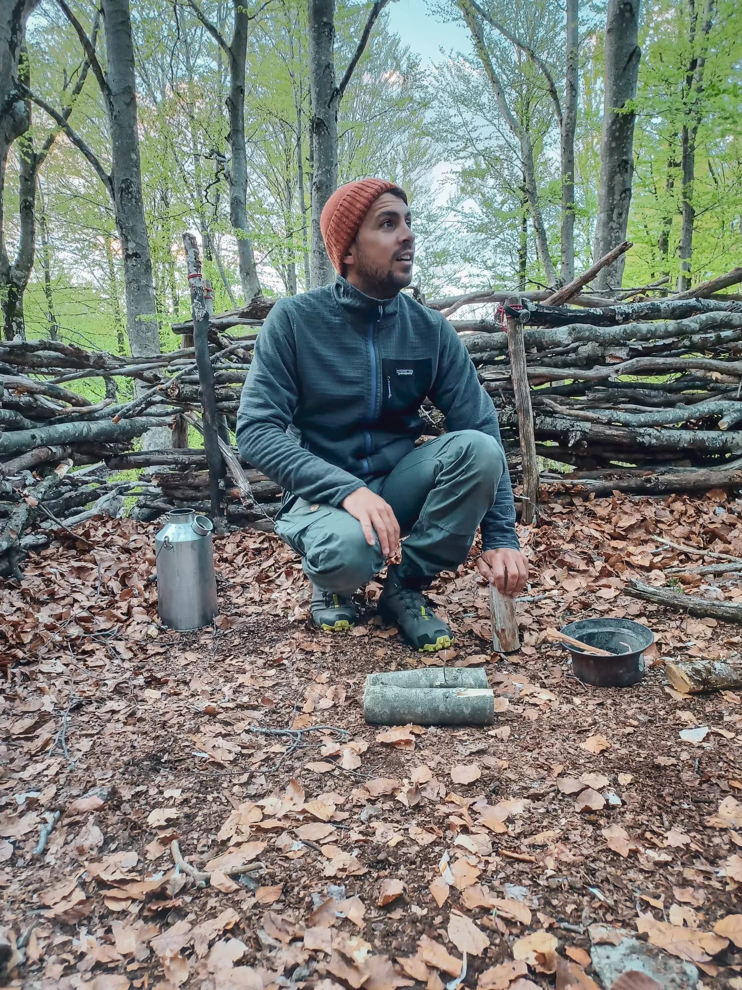 Een man in de wildernis, die bushcrafttechnieken leert, omringd door weelderige groene bomen.