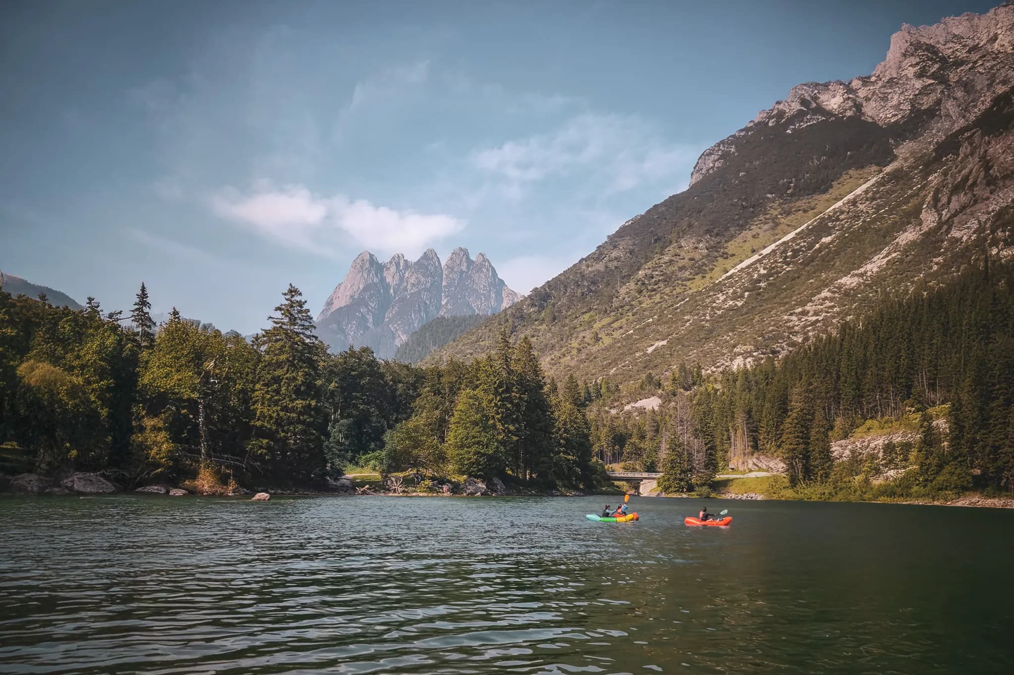 Deux packrafts glissent sur un lac tranquille, entouré de montagnes majestueuses et de forêts verdoyantes.