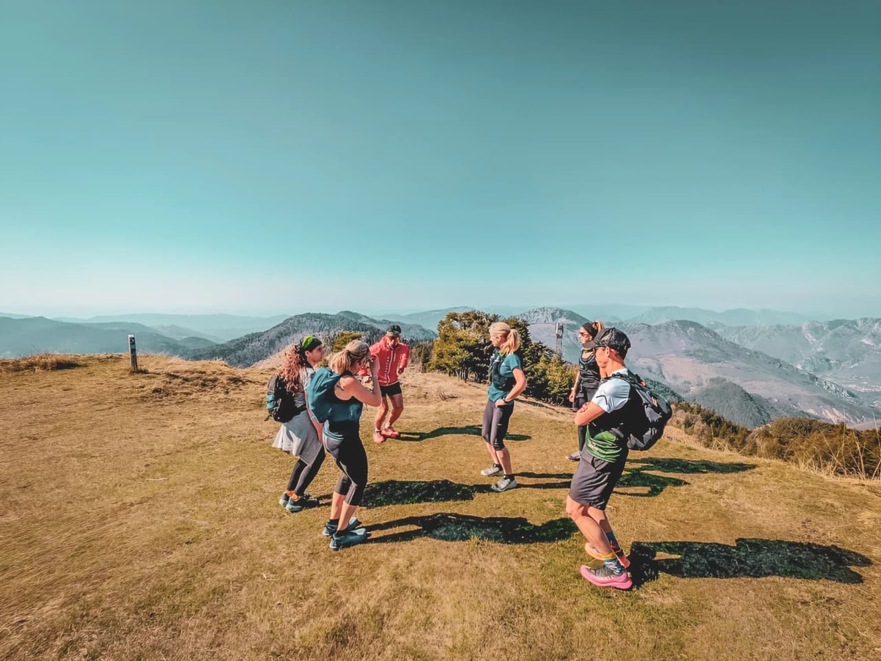 Groupe de coureurs enthousiastes sur un sommet ensoleillé, avec des montagnes en toile de fond.