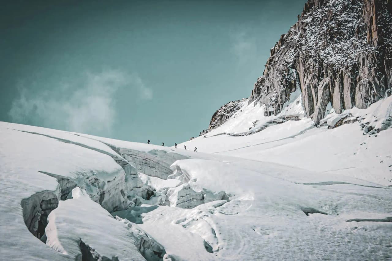 A team of mountaineers make their way across a glistening glacier under an azure sky.