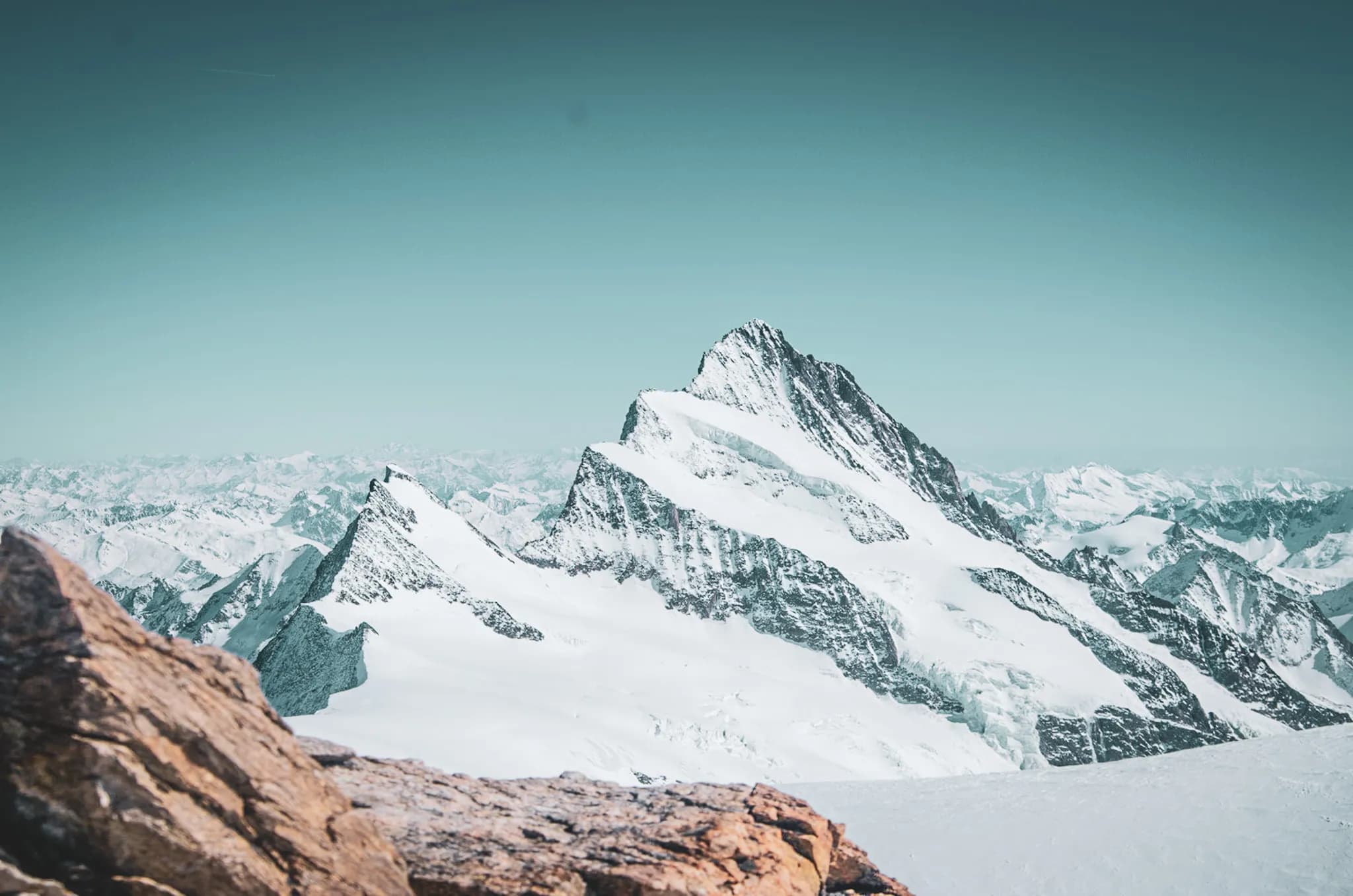 An impressive mountain landscape, dominated by a steep, snow-capped peak, rises majestically against a blue-green sky. The surrounding mountains of the Bernese Alps.