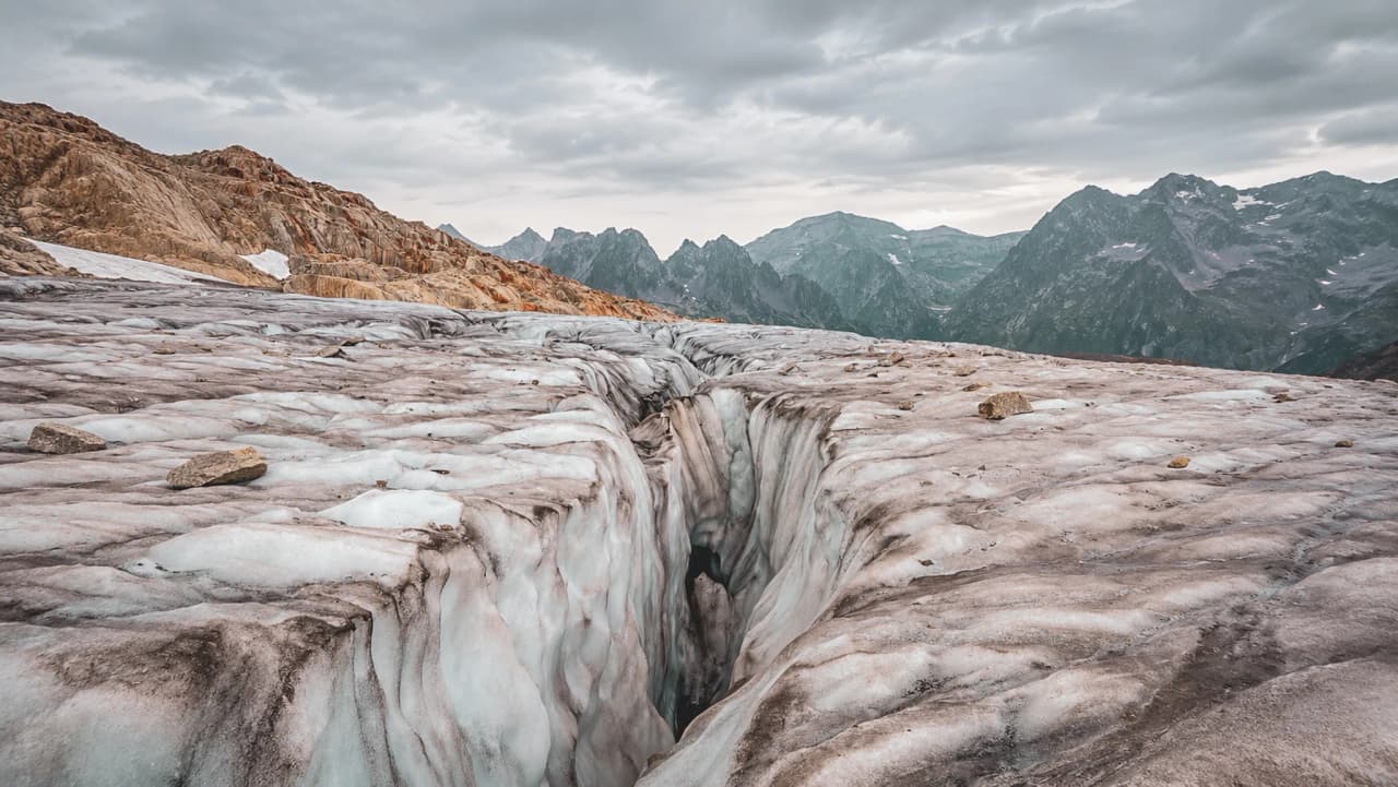 Glacier majestueux au sommet des Alpes, crevasses impressionnantes sous un ciel nuageux.